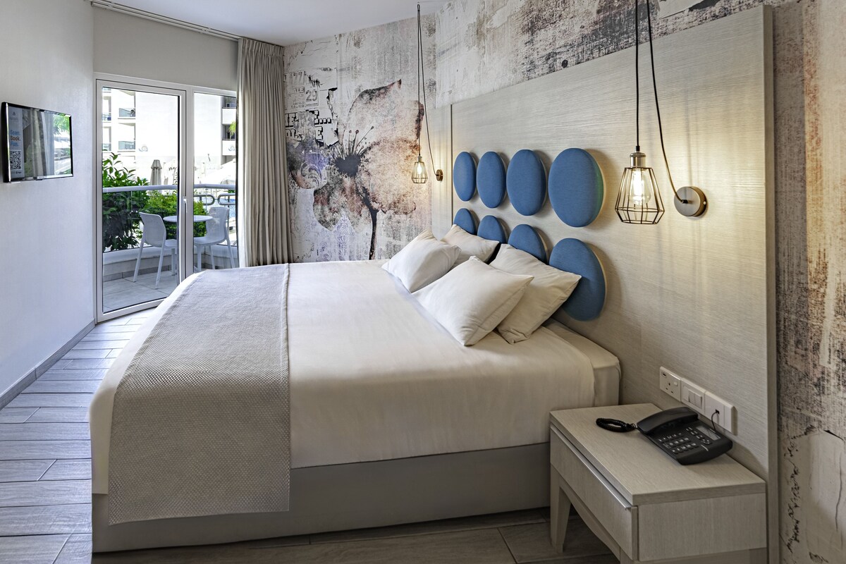 Ein modernes Hotelzimmer mit einem großen Bett, einem Nachttischtelefon und Blick auf den Balkon.