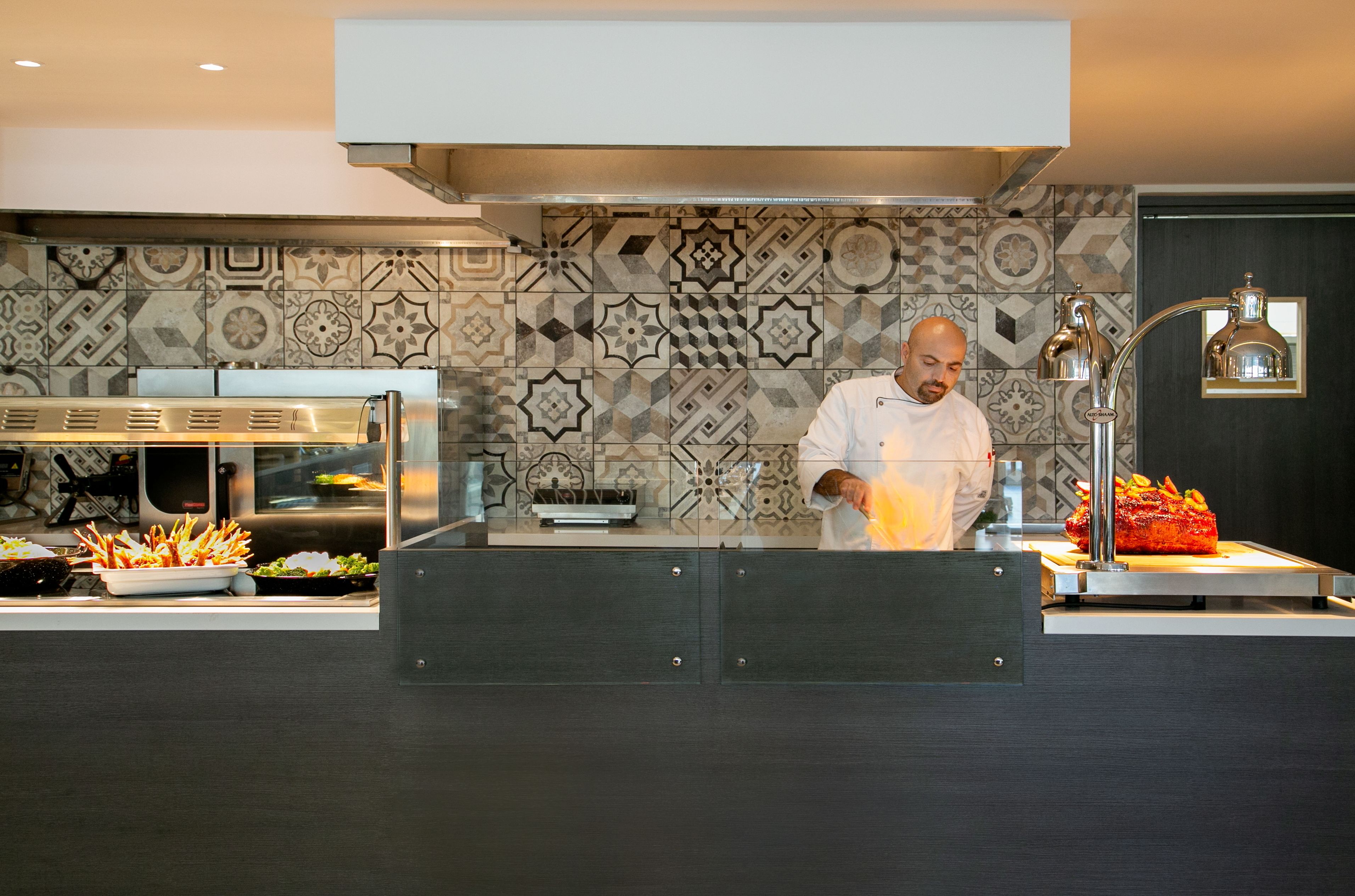 A chef preparing food in a modern kitchen with patterned tiles and stainless steel appliances.
