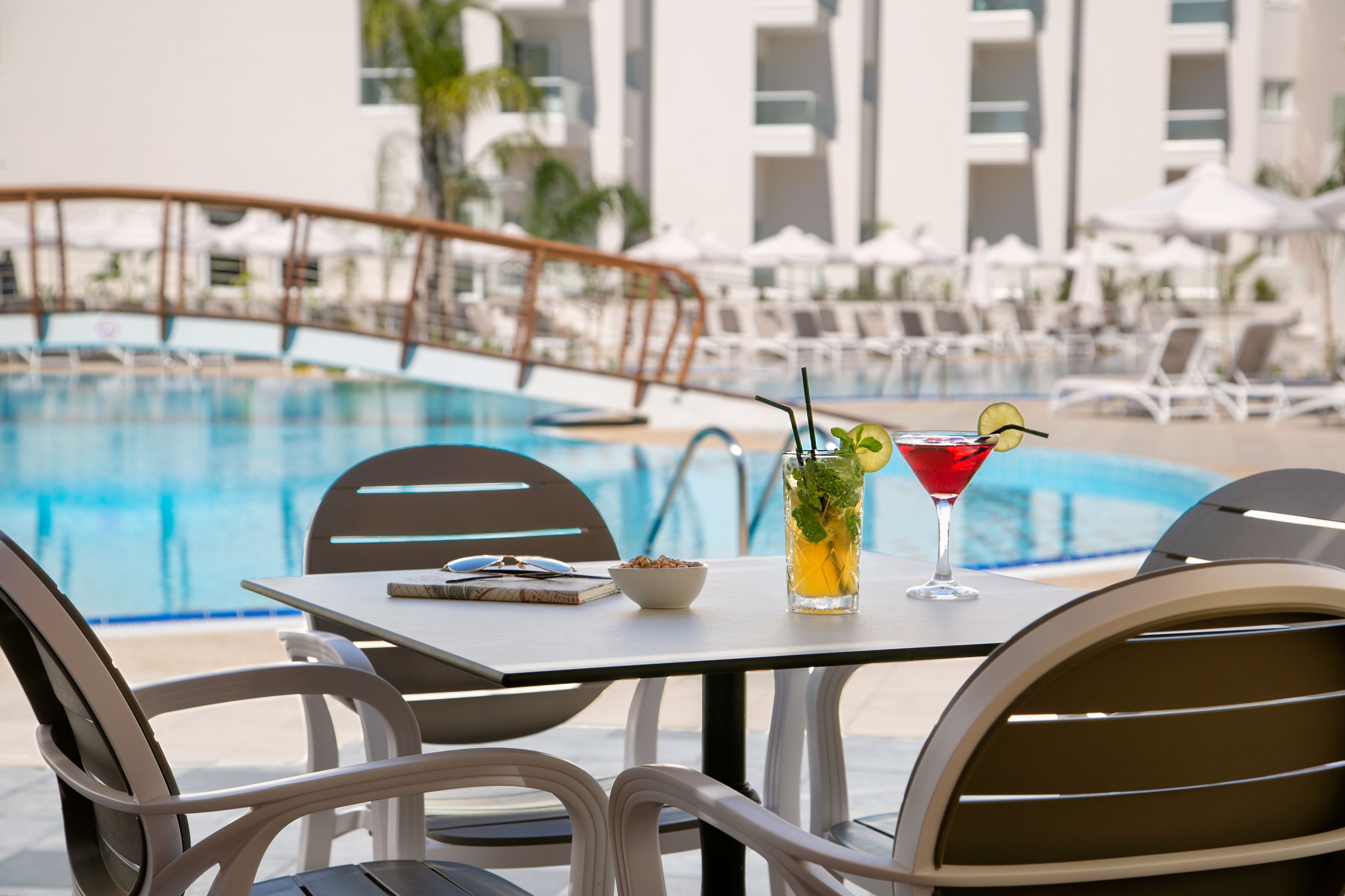 Une table au bord de la piscine, avec une boisson, un bol de collations et un livre.