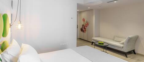 A modern hotel room with a large bed, a sofa, a small table with fruit, and a decorative flower arrangement.