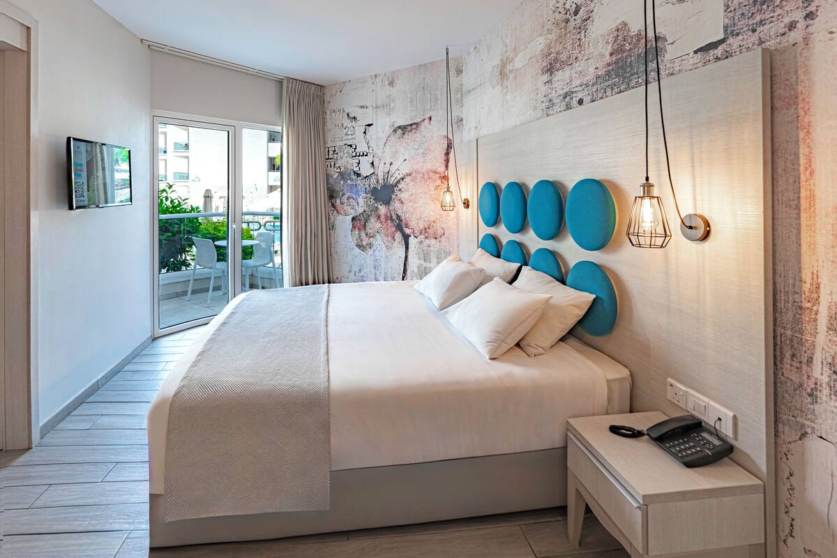 Une chambre d’hôtel moderne avec un grand lit, une table de chevet avec un téléphone et une vue sur le balcon.