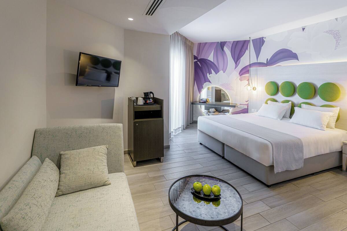 Une chambre d’hôtel moderne équipée d’un lit, d’un canapé, d’une télévision, d’une machine à café et d’une table avec des pommes.