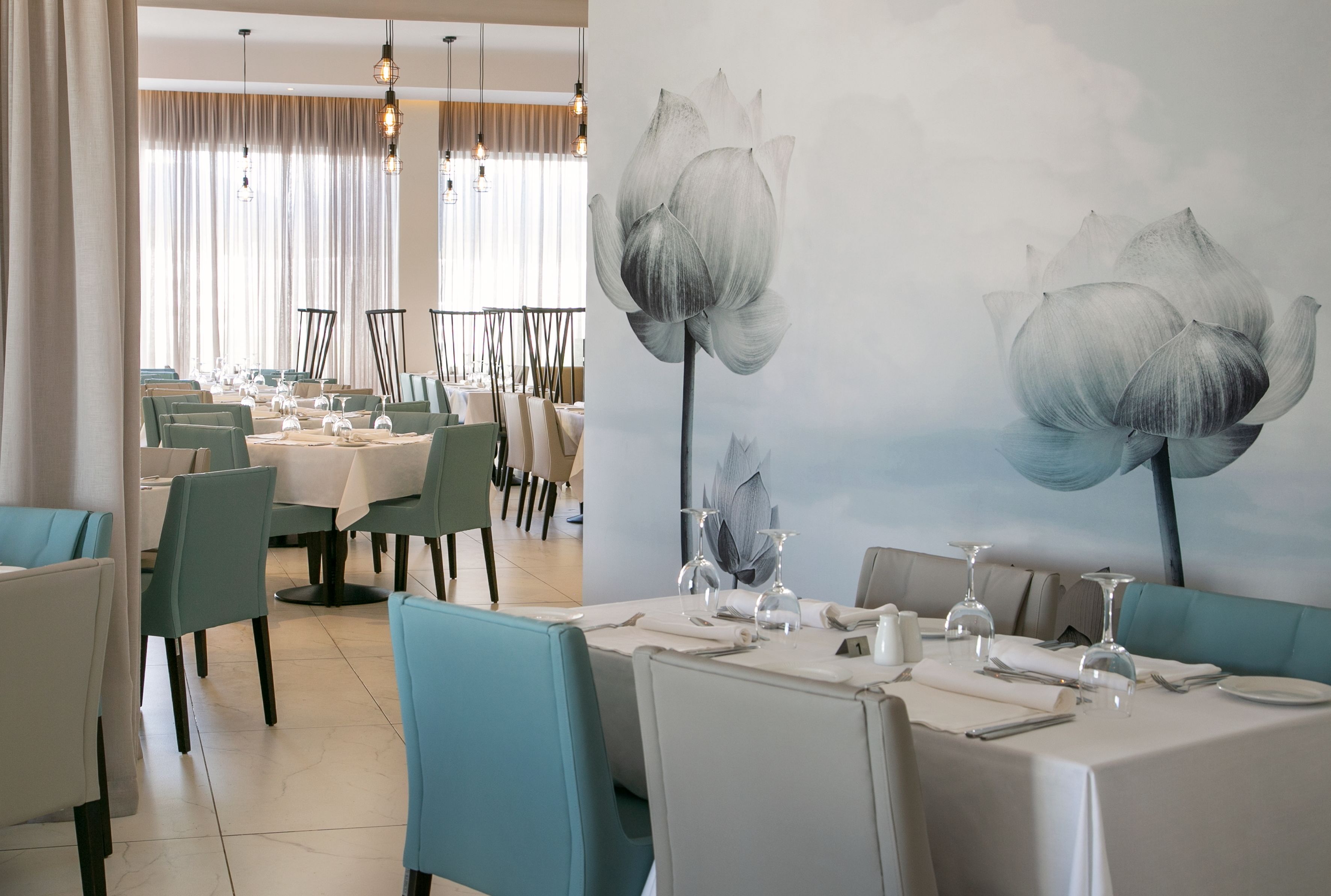 A restaurant with tables set for dining, a large floral mural on the wall, and a modern chandelier.