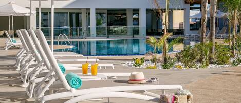 A poolside area with lounge chairs, a pool, and a building in the background.