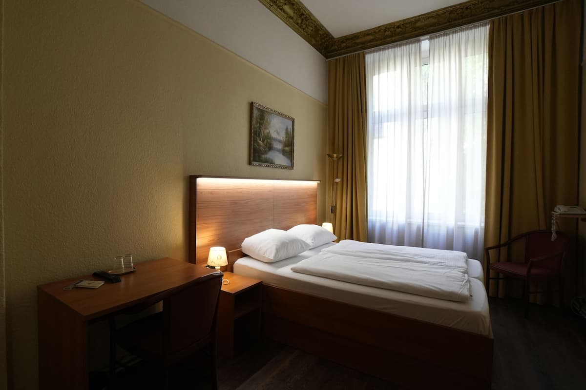 A hotel room with a bed, bedside table, lamp, and a painting on the wall.