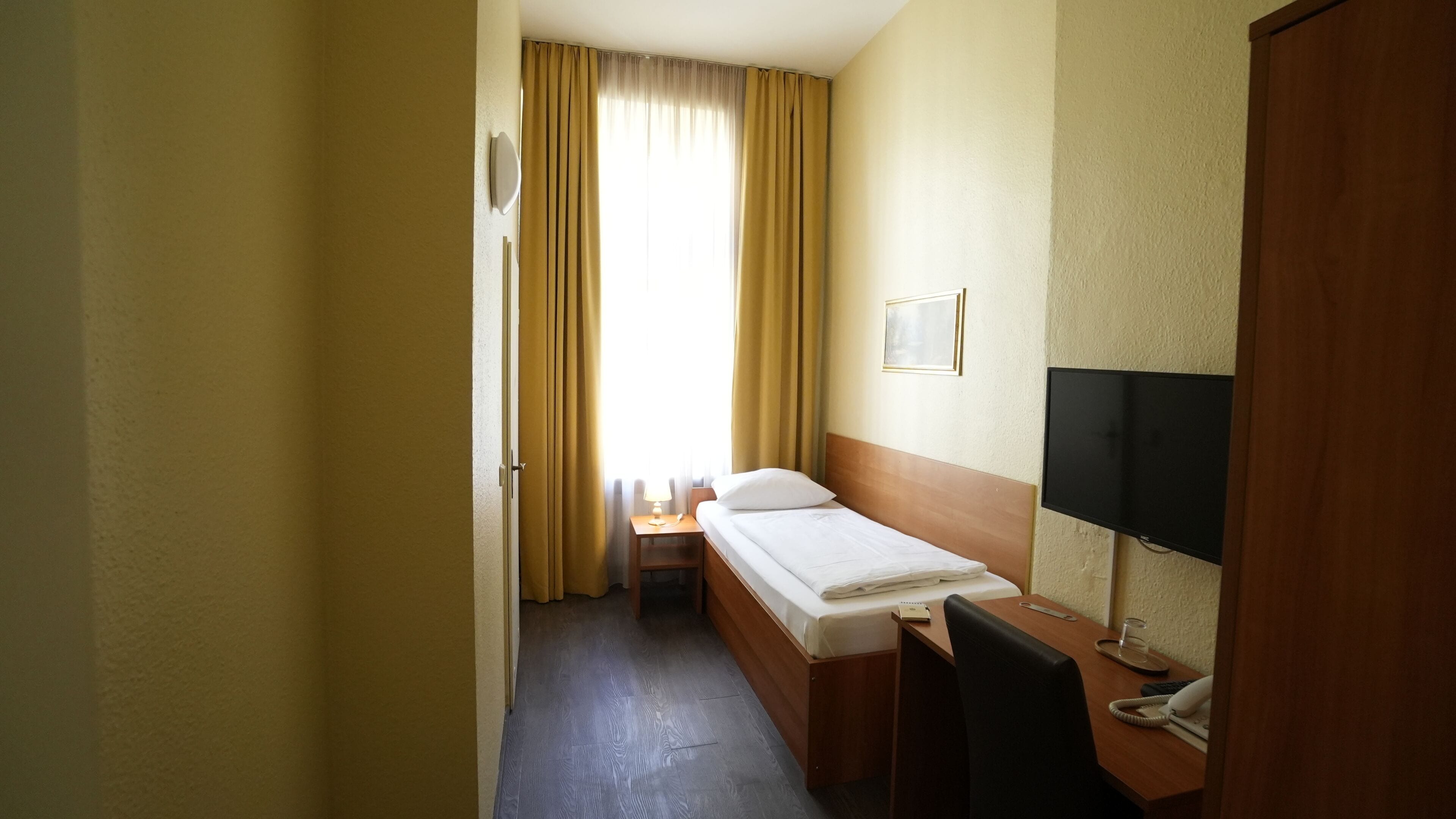 Una camera d'albergo con un letto, un comodino, una lampada, televisore e una scrivania con sedia.