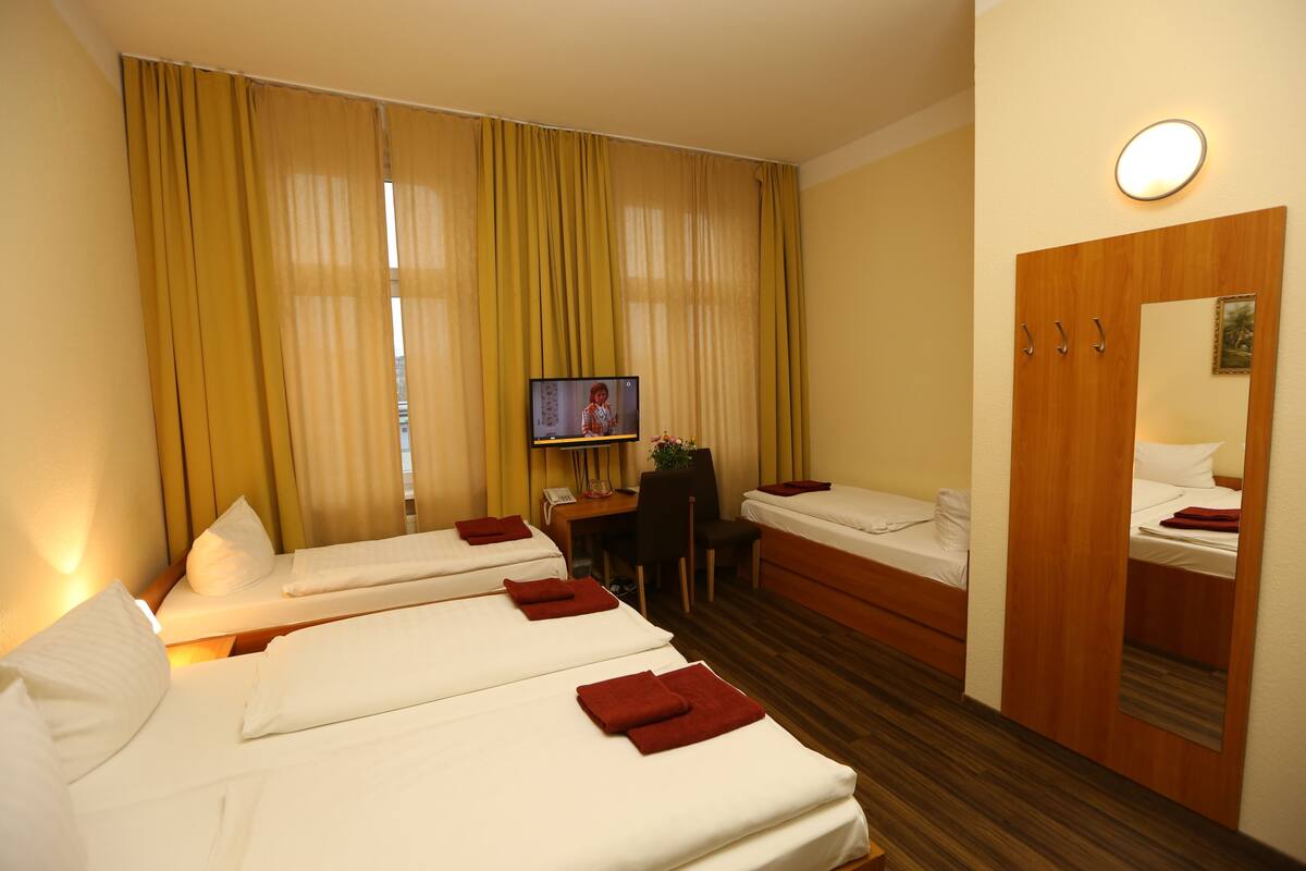 A hotel room with three single beds, a desk with a chair, a television, and a wardrobe.