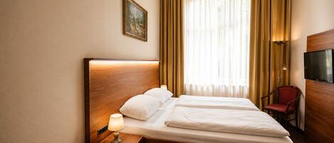 A hotel room with a double bed, a bedside table with a lamp, a chair, and a television on the wall.