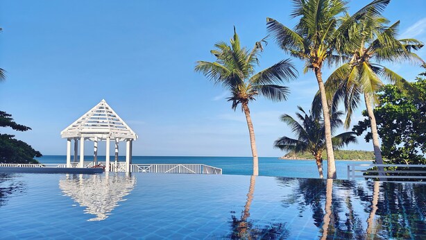 An infinity pool with a white gazebo and palm trees, overlooking a clear blue sea. - Bhundhari Resort & Villas Samui (Koh Samui)