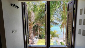 A bathroom with a bathtub, a window with a view of a pool and palm trees, and a door with a handle. - Bhundhari Resort & Villas Samui (Koh Samui)