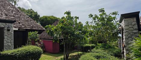 A courtyard with a stone building, a wooden structure, and lush greenery.