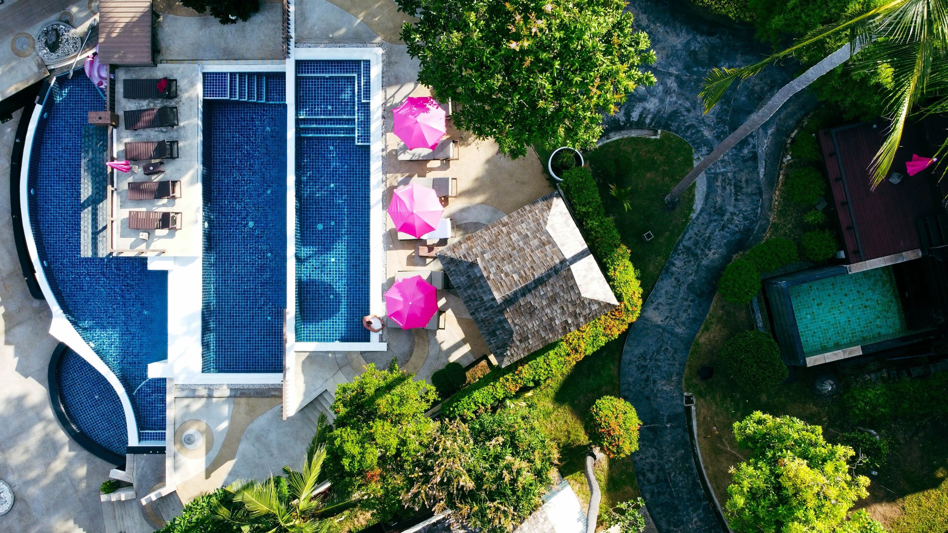Vista aérea de um resort com uma grande piscina, espreguiçadeiras e guarda-sóis.