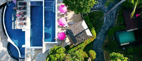 Vista aérea de um resort com uma grande piscina, espreguiçadeiras e guarda-sóis.