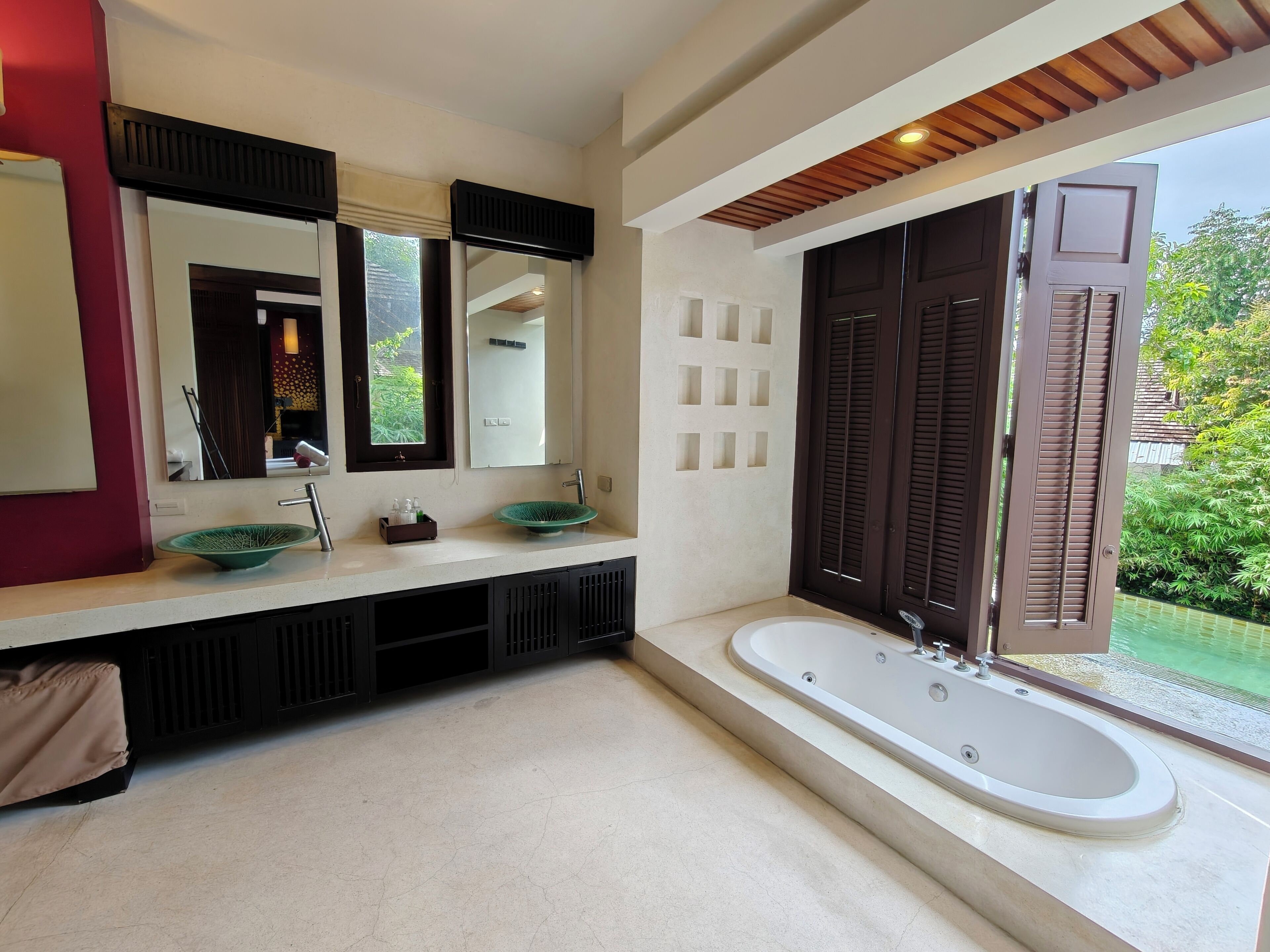 Un baño moderno con un espejo grande, dos lavamanos, una bañera y vistas a zonas verdes al exterior.