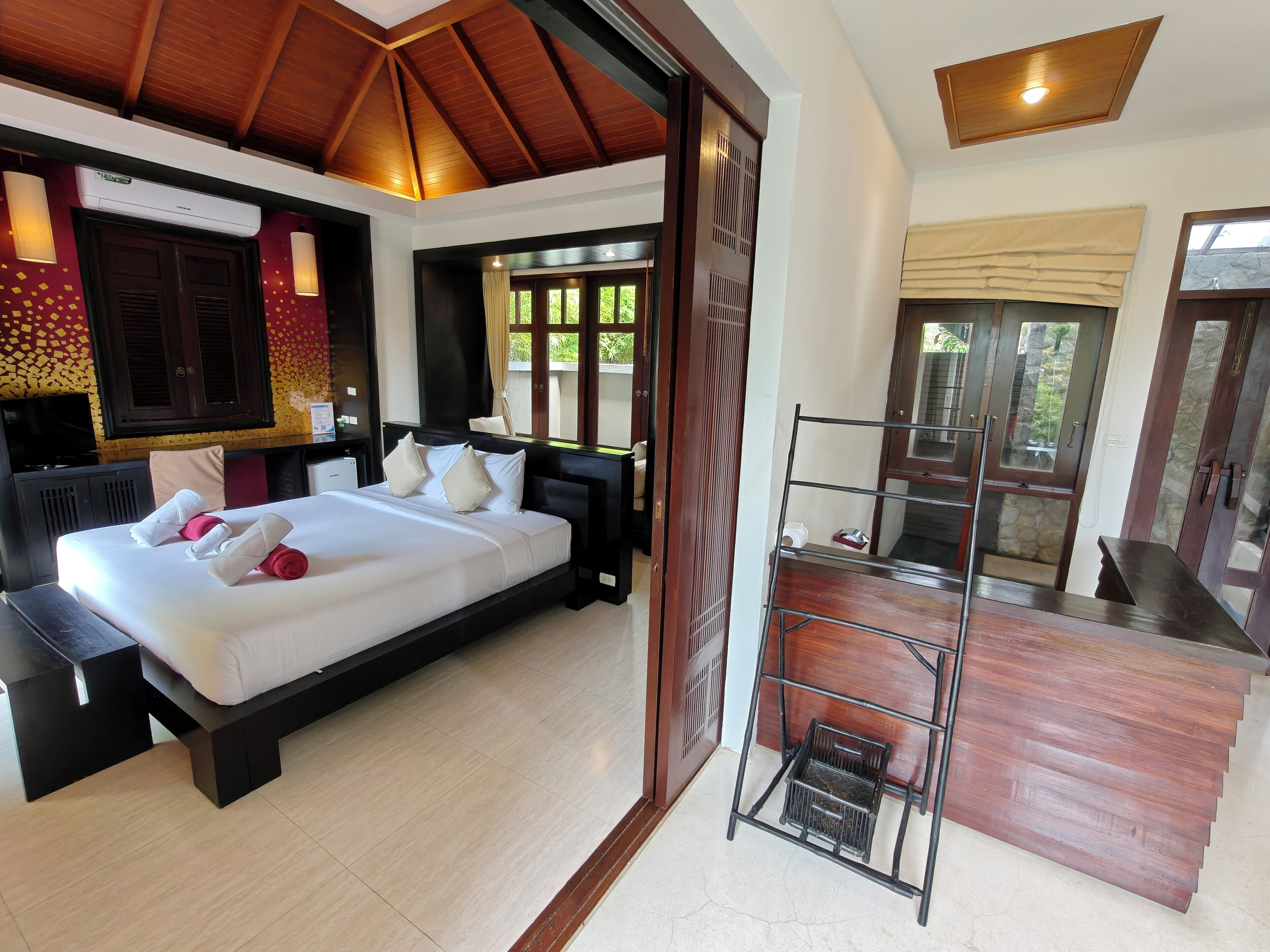 A hotel room with a large bed, a desk, a chair, a TV, and a balcony with a view.