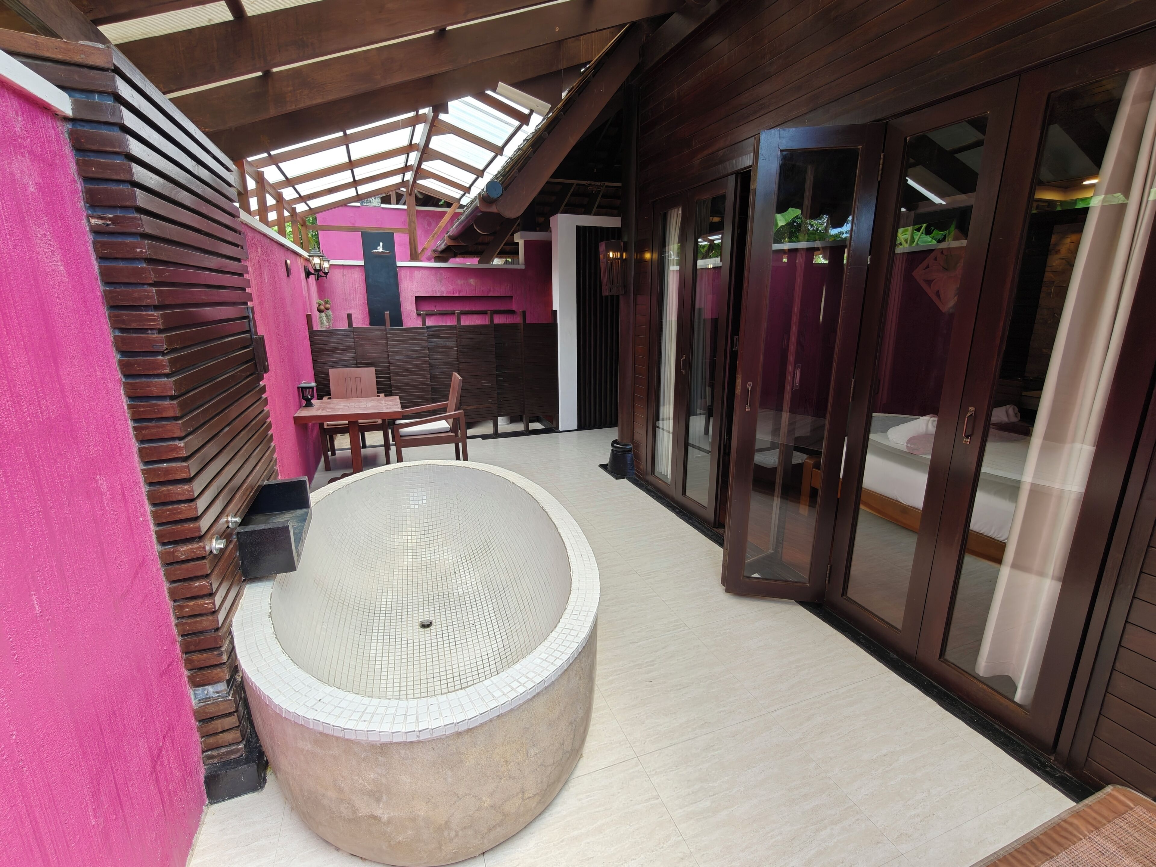 A spa area with a large circular hot tub, wooden flooring, and a glass-enclosed room with a bed.