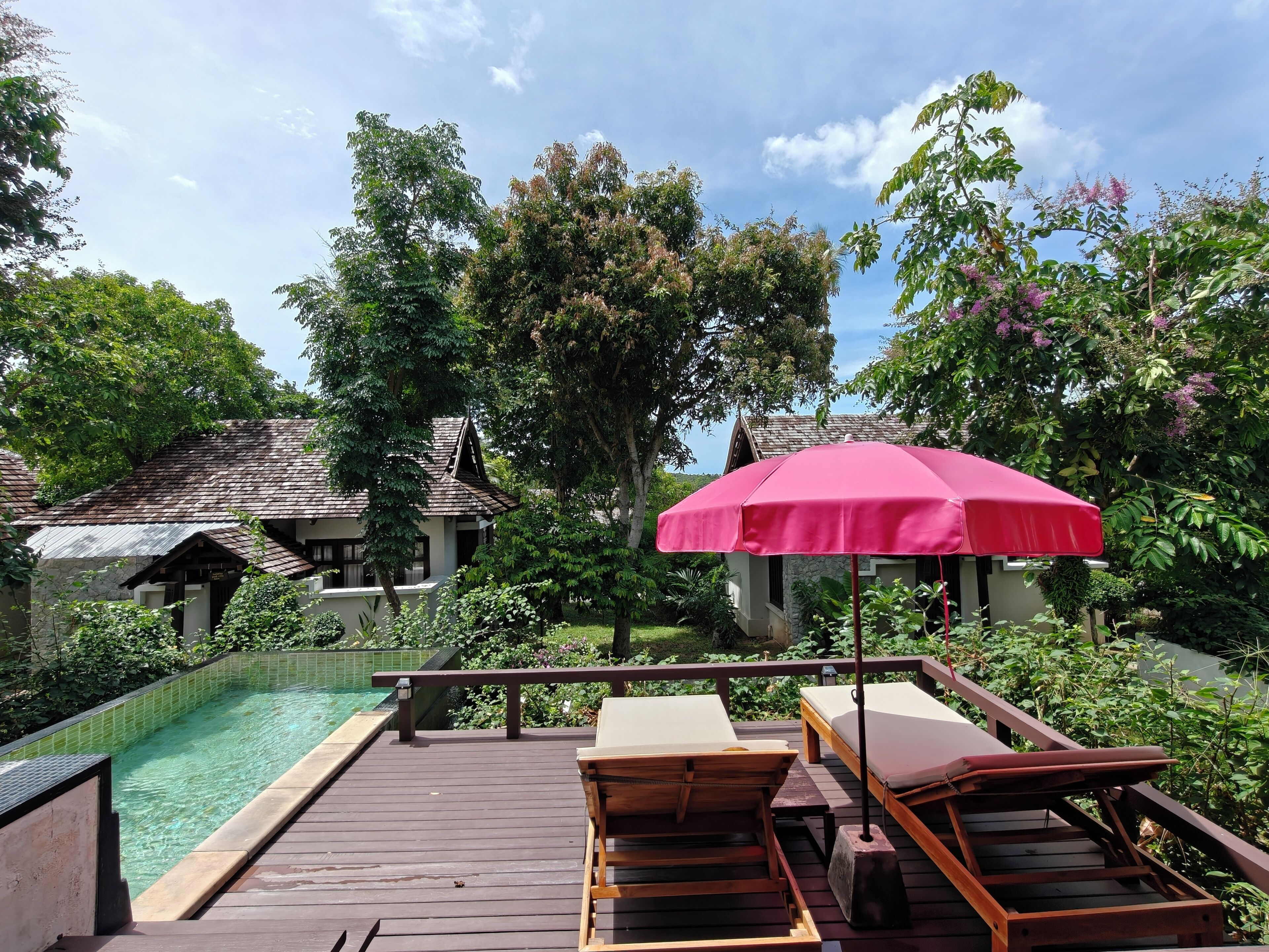 A wooden deck with a pool, lounge chairs, and a red umbrella.