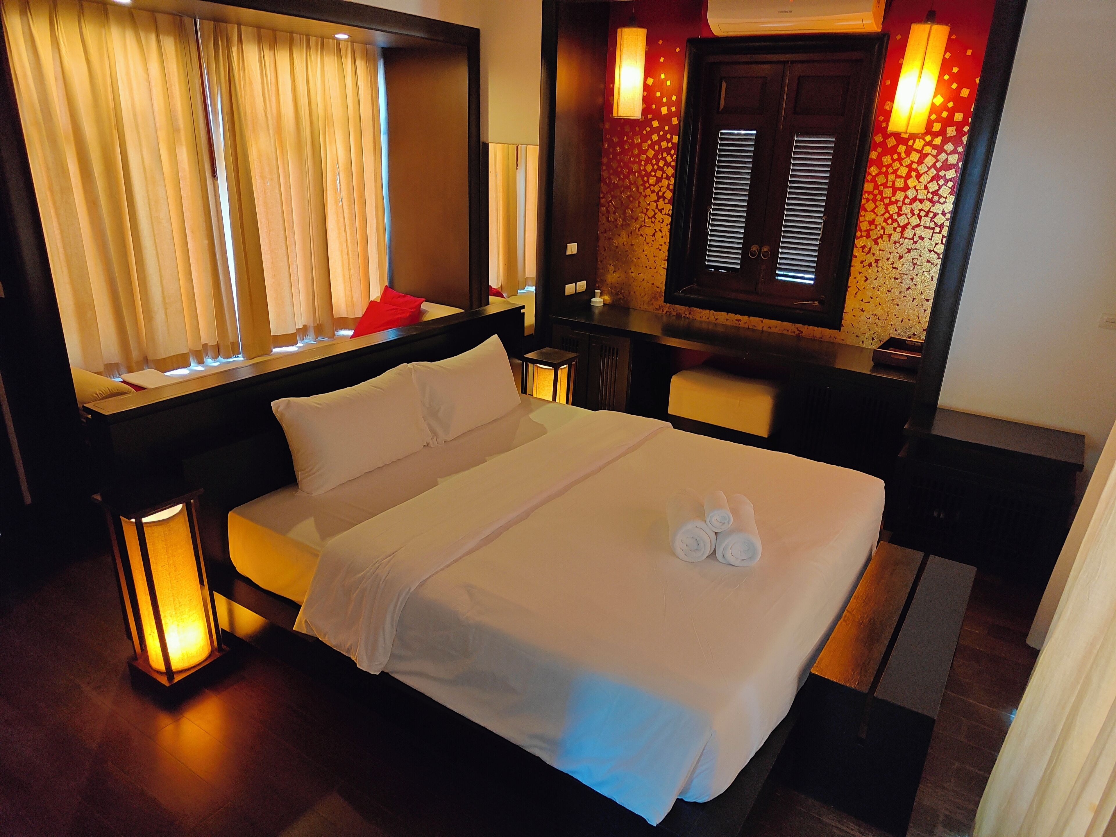 A hotel room with a large bed, bedside lamps, a mirror, a window with curtains, and a wall with a mosaic pattern.