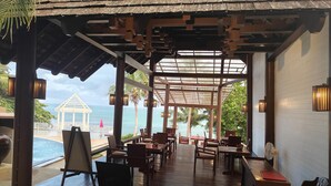 An open-air restaurant with a wooden deck, tables, and chairs, overlooking a pool and the sea. - Bhundhari Resort & Villas Samui (Koh Samui)