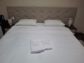 A neatly made bed with two pillows, a nightstand with a lamp, and two towels with text on them. - Hotel Vila Silia (Skopje)