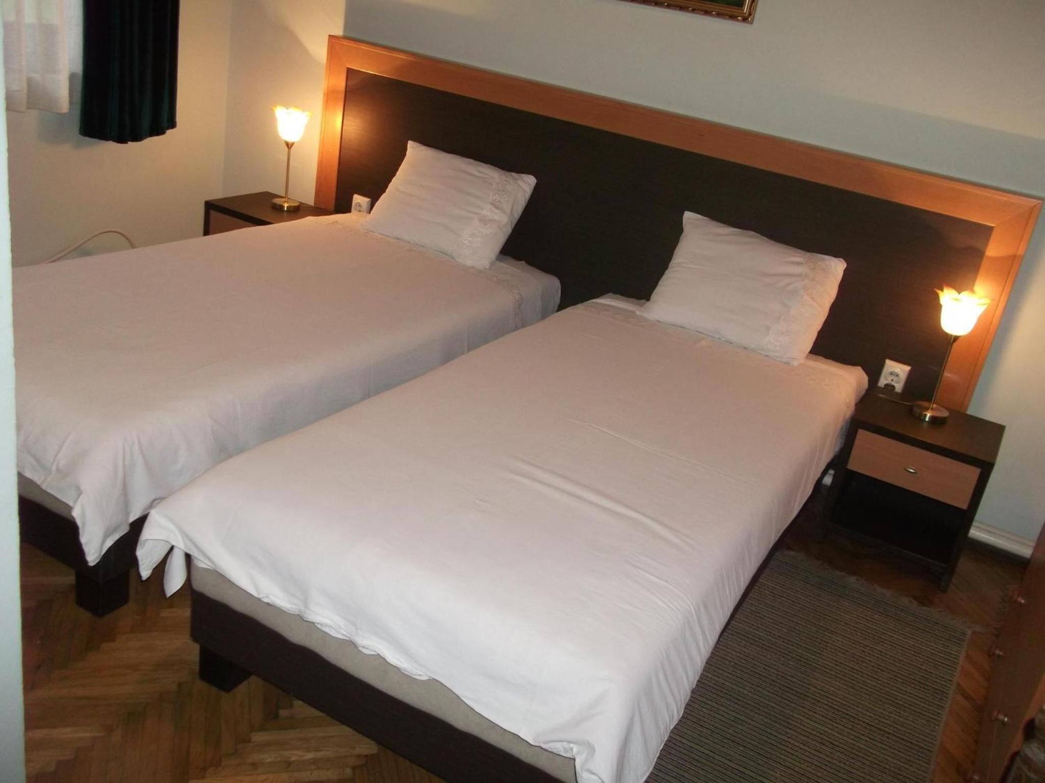 A hotel room with two single beds, each with a wooden headboard, white linens, and bedside lamps.