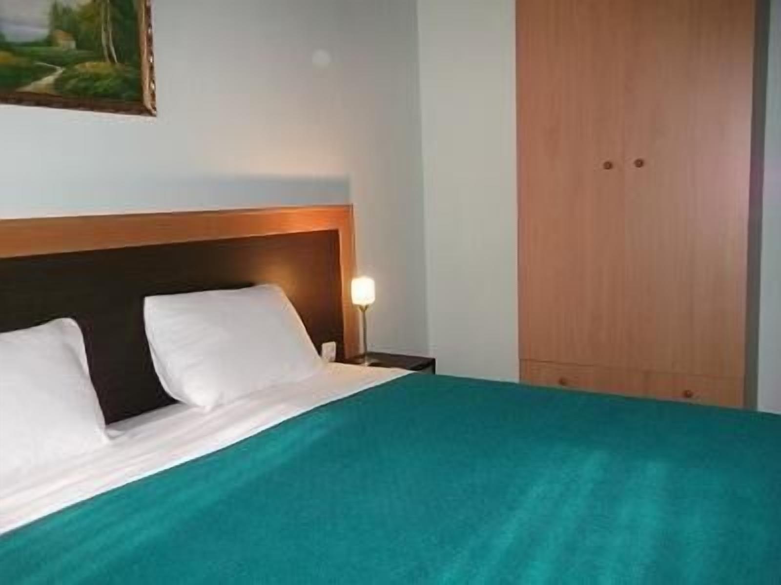Una habitación de hotel con una cama, una mesita de noche, una lámpara y un armario de madera.