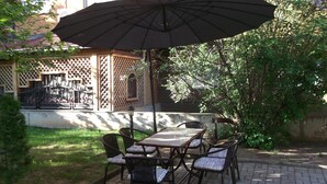 An outdoor patio with a table and chairs, a large umbrella, and a wooden fence. - Hotel Vila Silia (Skopje)