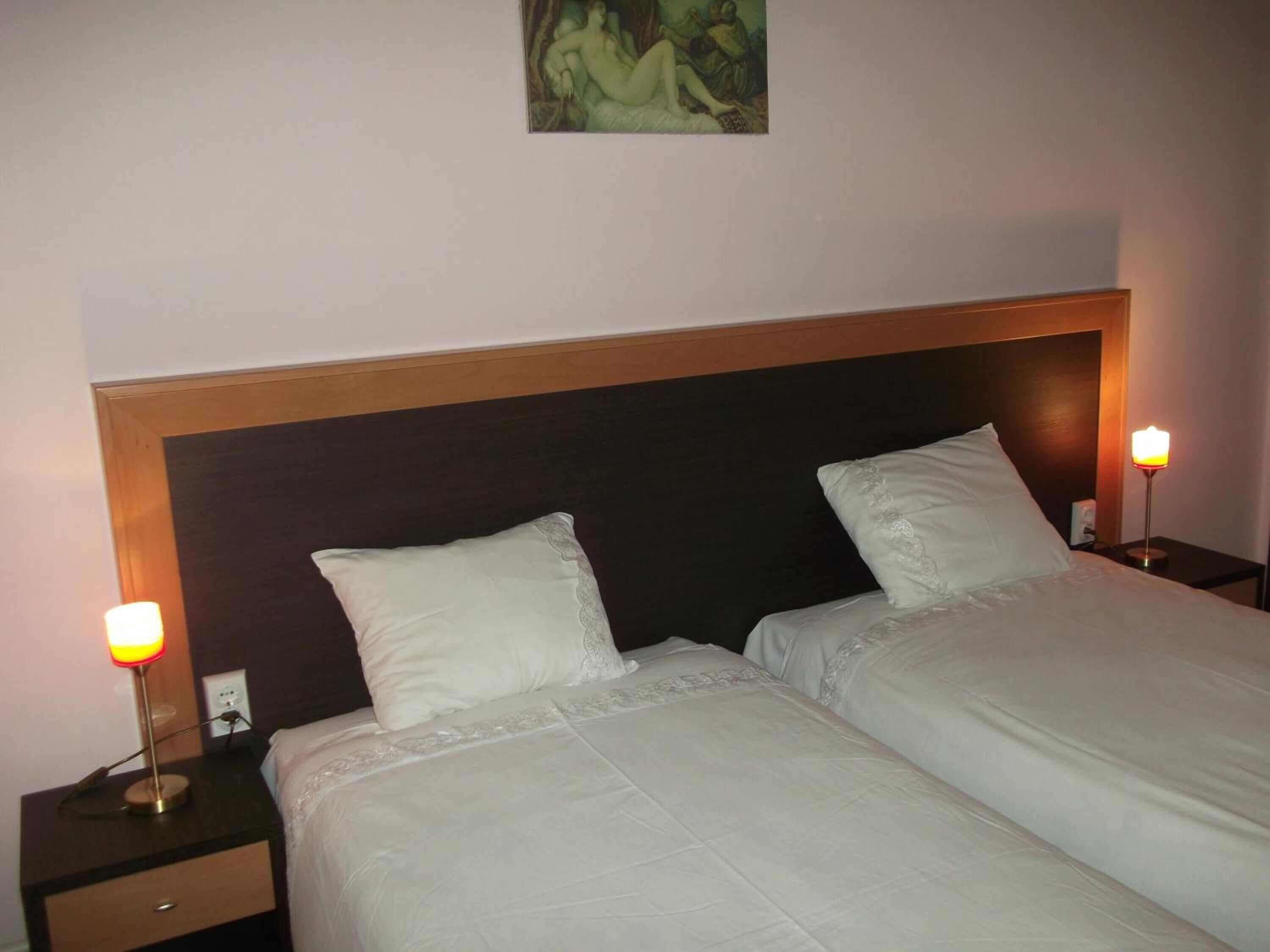Una habitación de hotel con dos camas individuales, una mesita de noche con lámpara y un cuadro en la pared.