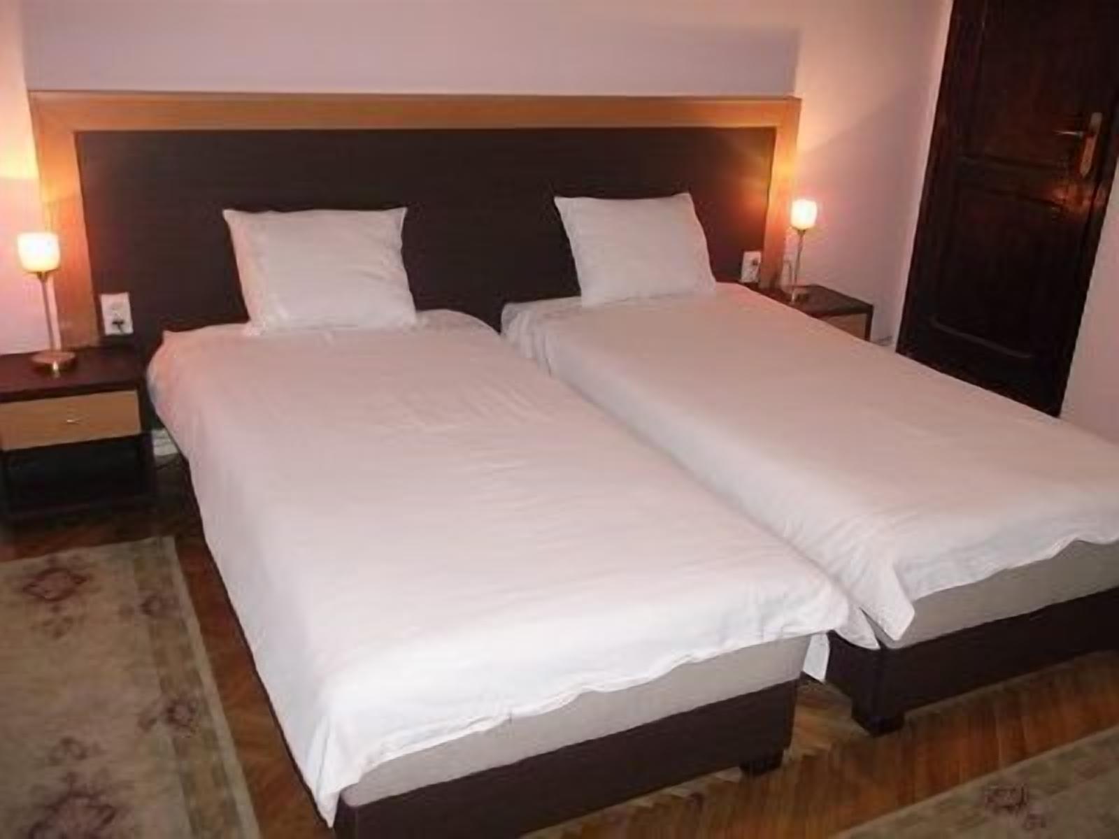A double bed with white linens and a wooden headboard. There are two bedside tables with lamps.