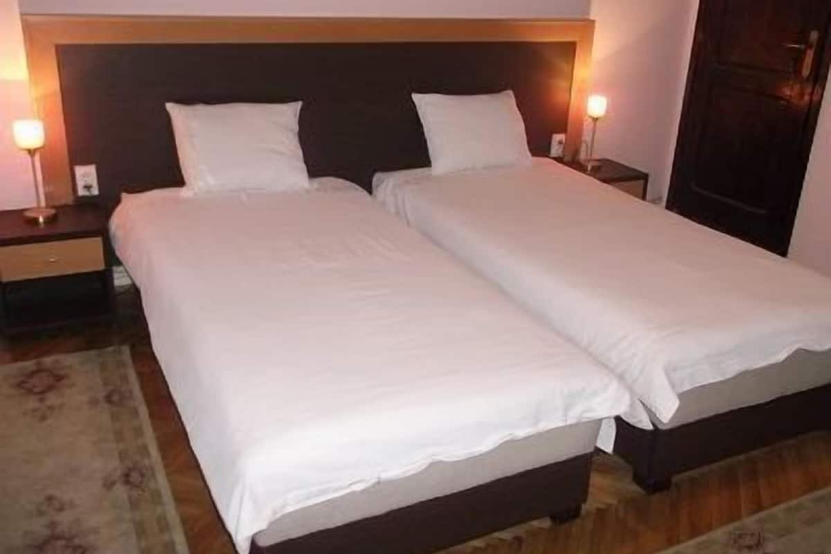 Un lit double avec du linge de lit blanc et une tête de lit en bois. Il y a deux tables de chevet avec des lampes.