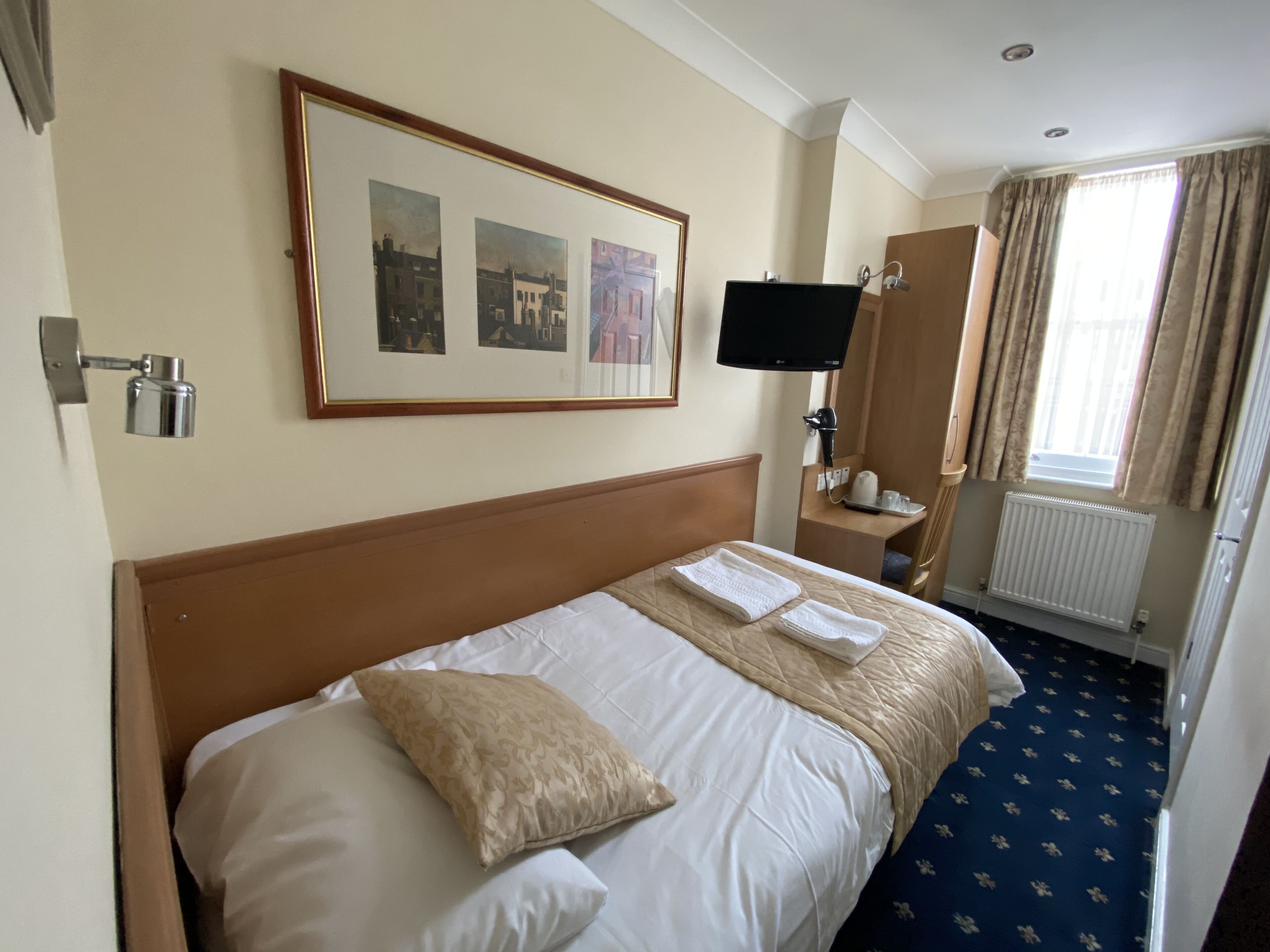 A hotel room with a large bed, a flat-screen TV, a desk with a lamp, and a window with curtains.