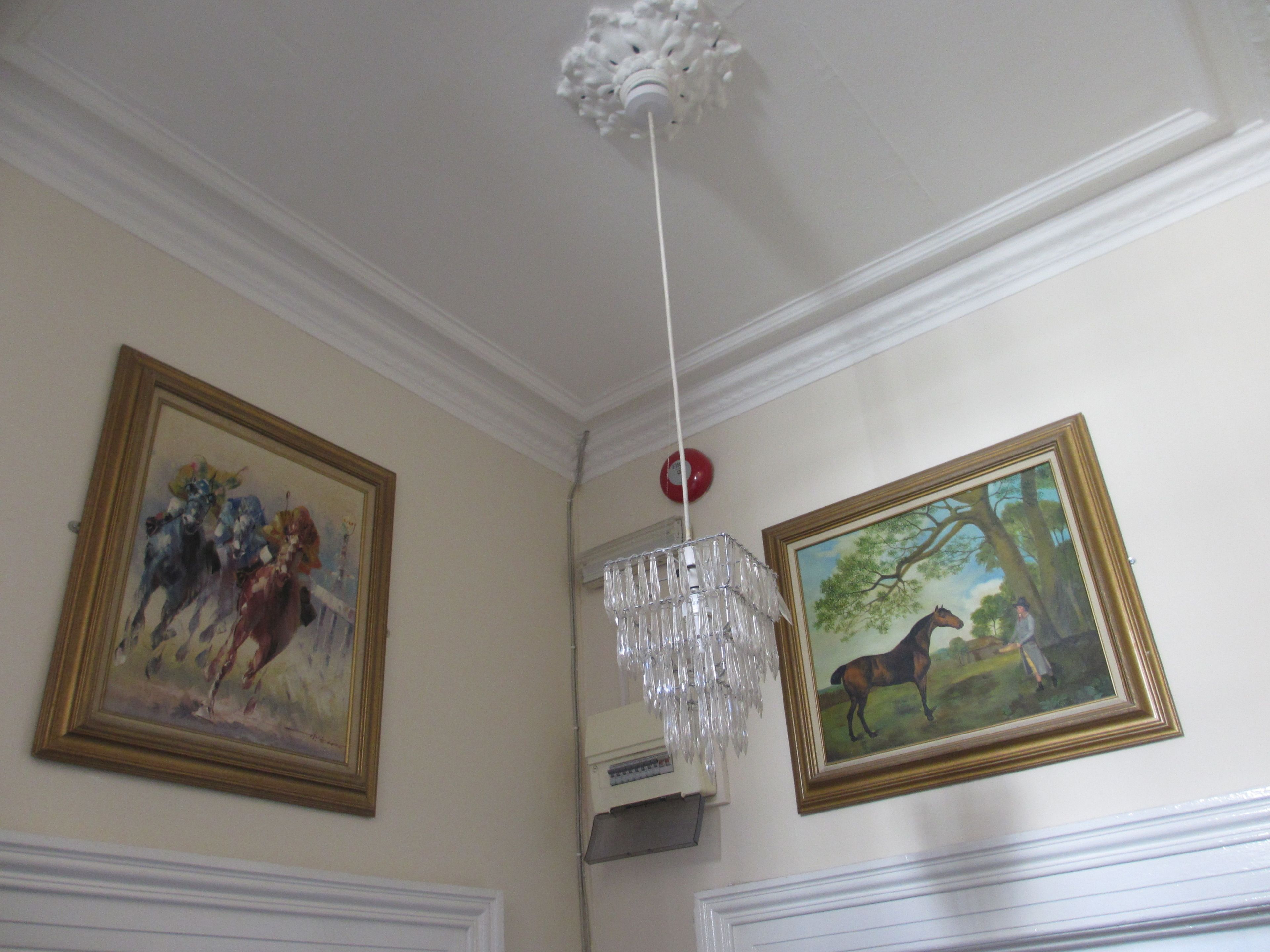 A room with two framed paintings, a chandelier, and a ceiling fan.