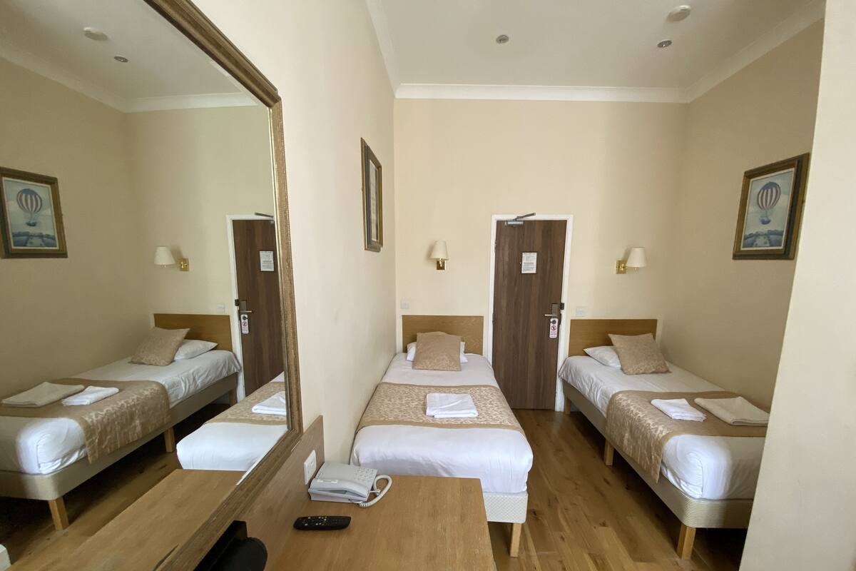 A hotel room with two single beds, a wooden desk, a telephone, and a mirror.