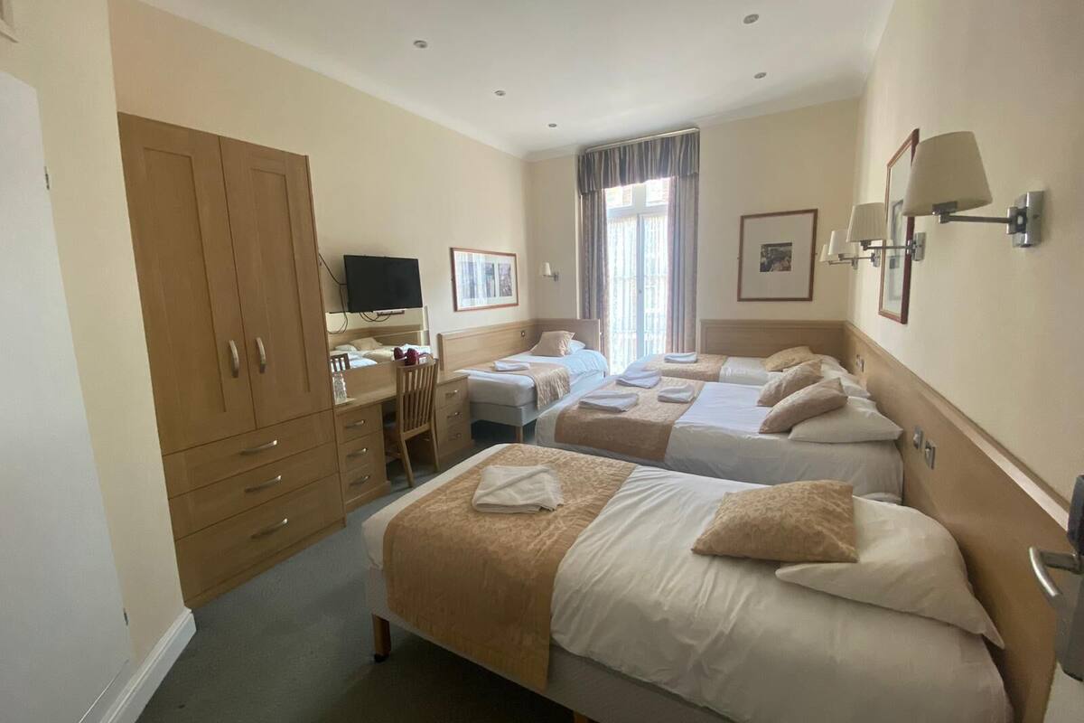 A hotel room with two beds, a desk, a chair, a television, and a window with curtains.