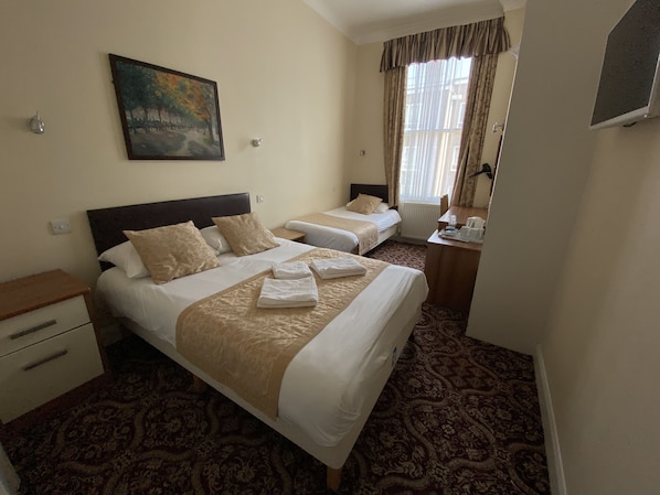 A hotel room with two beds, a painting on the wall, a desk with a chair, and a window with curtains.