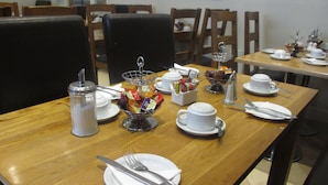 A dining table set with white plates, cups, and cutlery, along with a sugar dispenser and a basket of tea bags. - Belvedere Hotel (London)
