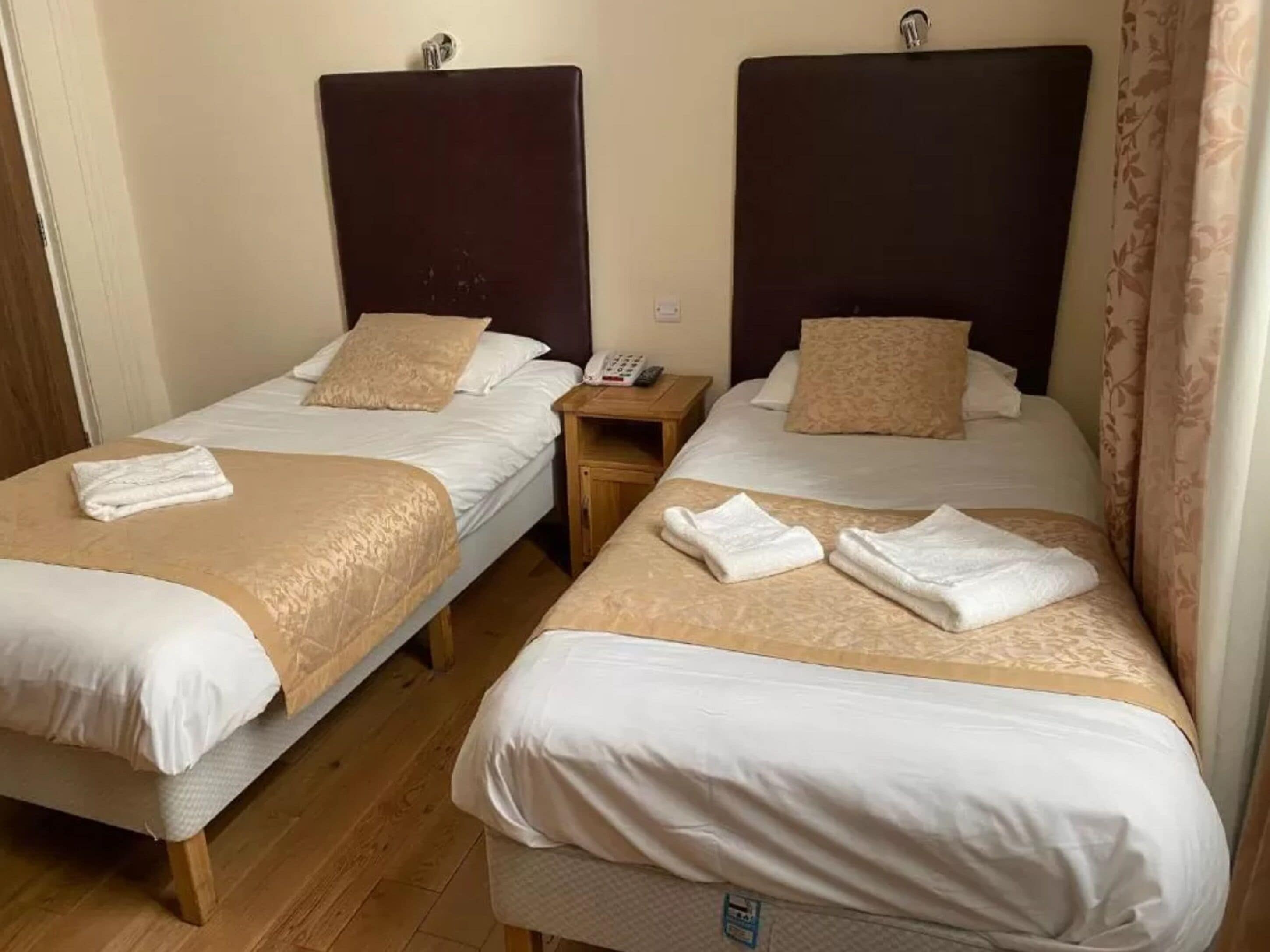 Deux lits jumeaux avec des têtes de lit, une table de chevet avec un téléphone et une serviette pliée sur chaque lit.