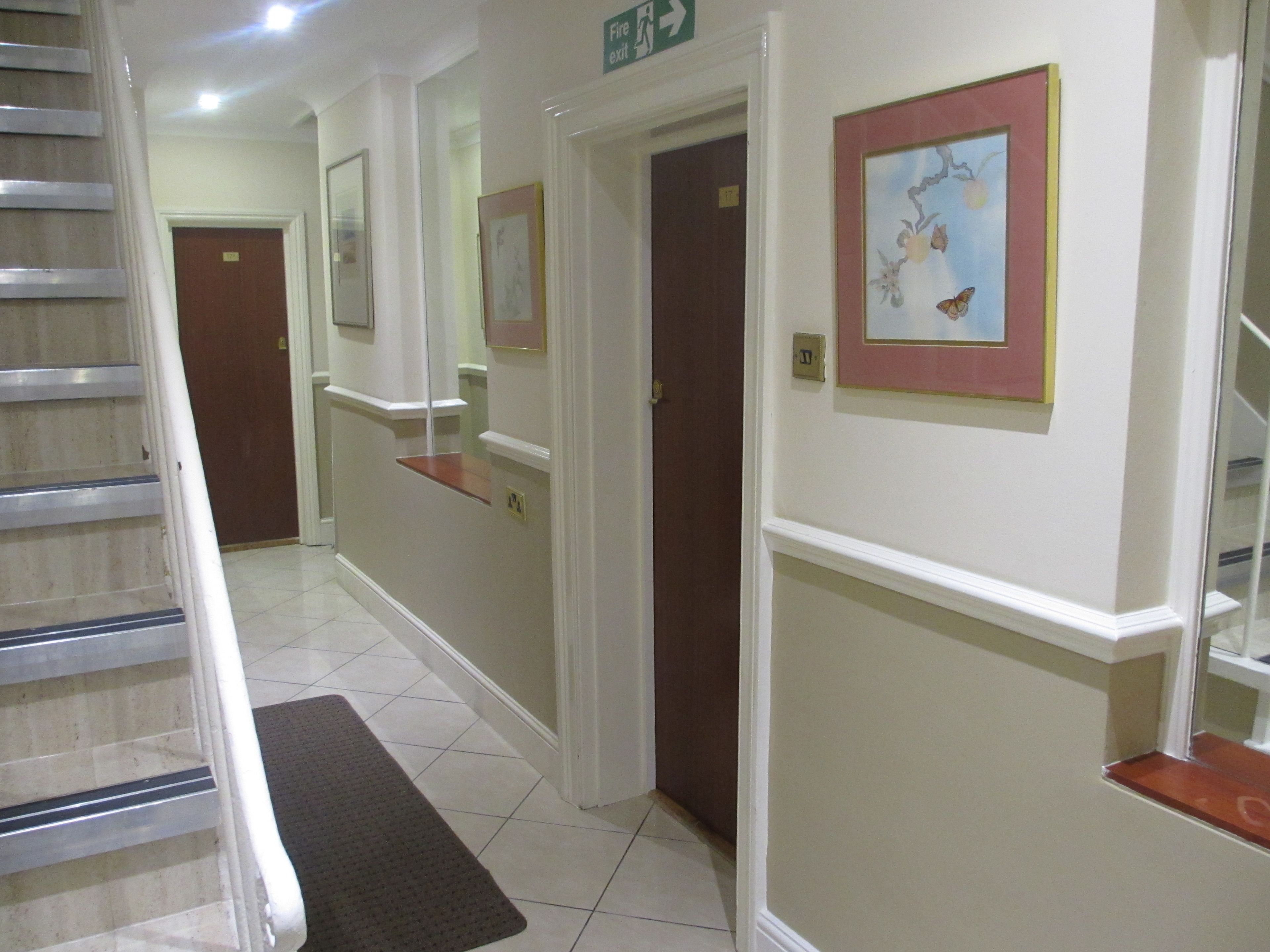 A hotel hallway with a staircase, a fire exit sign, and framed artwork on the walls.