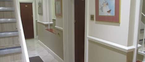 A hotel hallway with a staircase, a fire exit sign, and framed artwork on the walls.