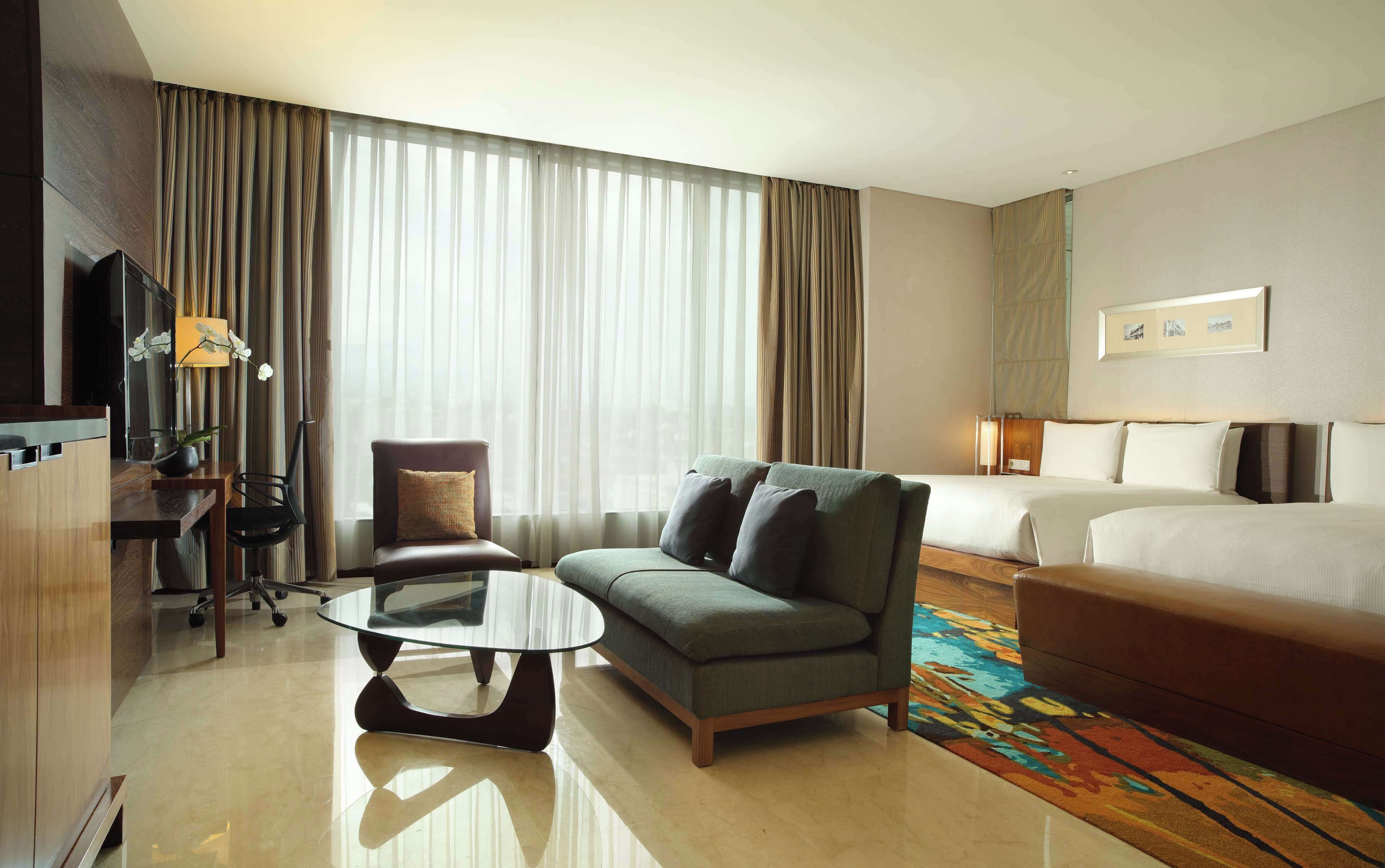 Habitación de hotel con cama, sofá, mesa de centro, televisor y escritorio.
