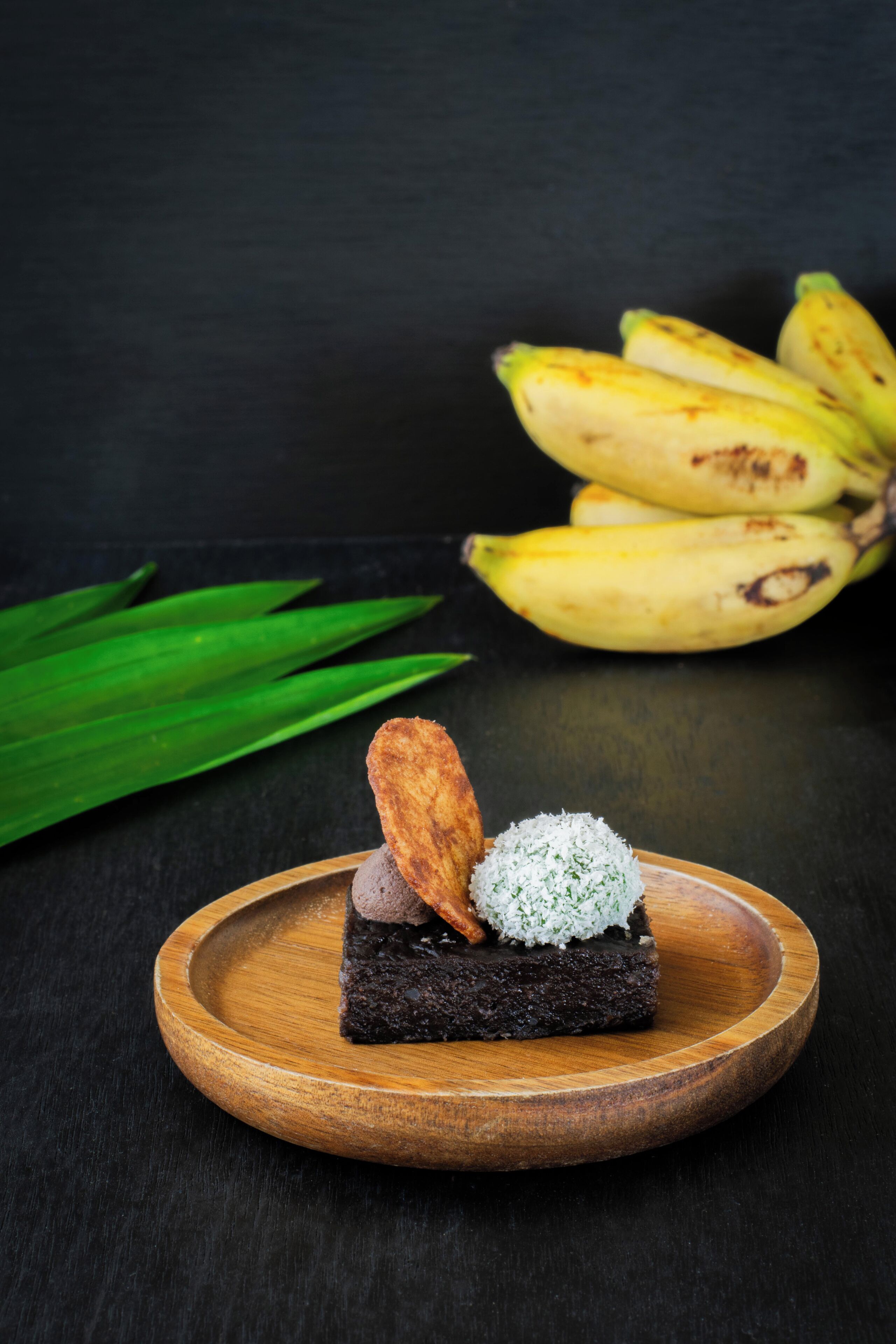 Un postre sobre un plato de madera, con plátanos al fondo.