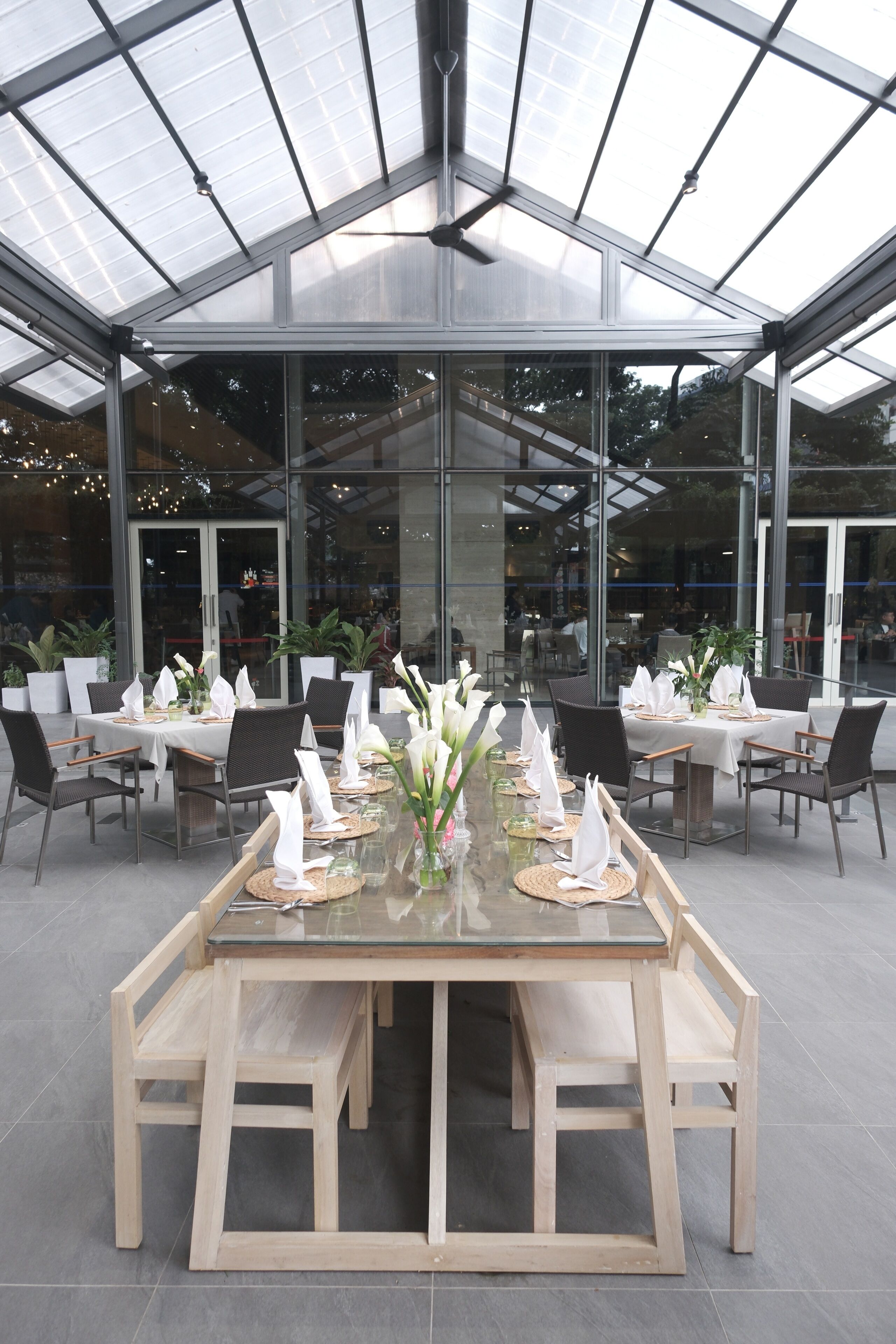 A restaurant with a glass-enclosed dining area, multiple tables set with white tablecloths, and chairs.