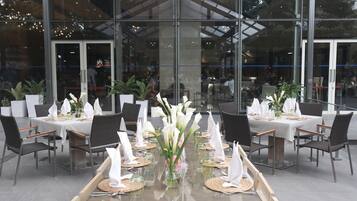 A restaurant with a glass-enclosed dining area, multiple tables set with white tablecloths, and chairs.