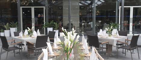 Un restaurant doté d’une salle à manger entièrement vitrée, de nombreuses tables recouvertes de nappes blanches et de chaises.