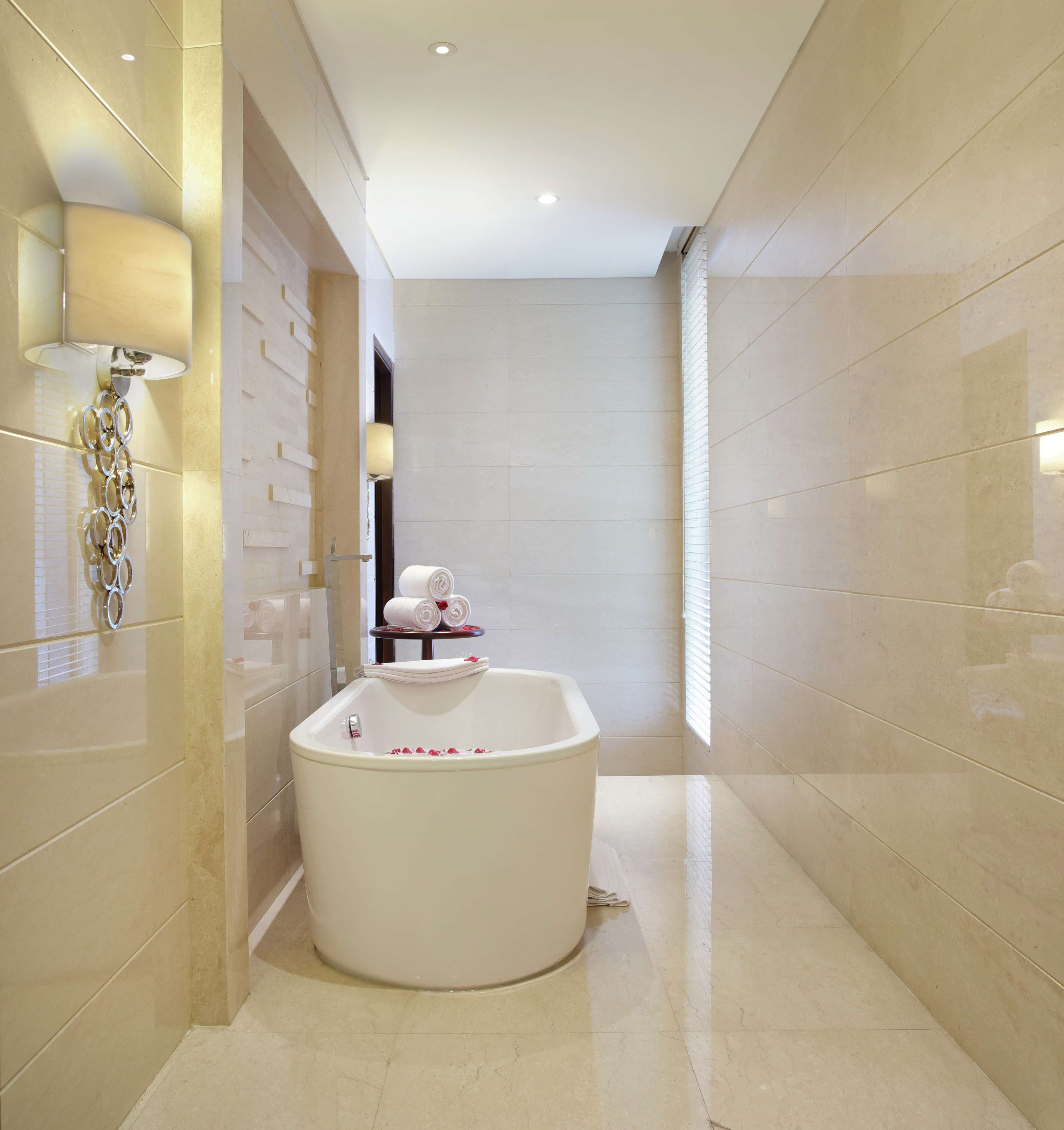 A modern bathroom with a freestanding bathtub, a wall-mounted light fixture, and a small table with towels.