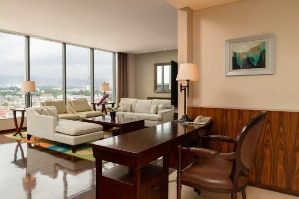 A hotel room with a large window, a sofa, a desk, and a chair.