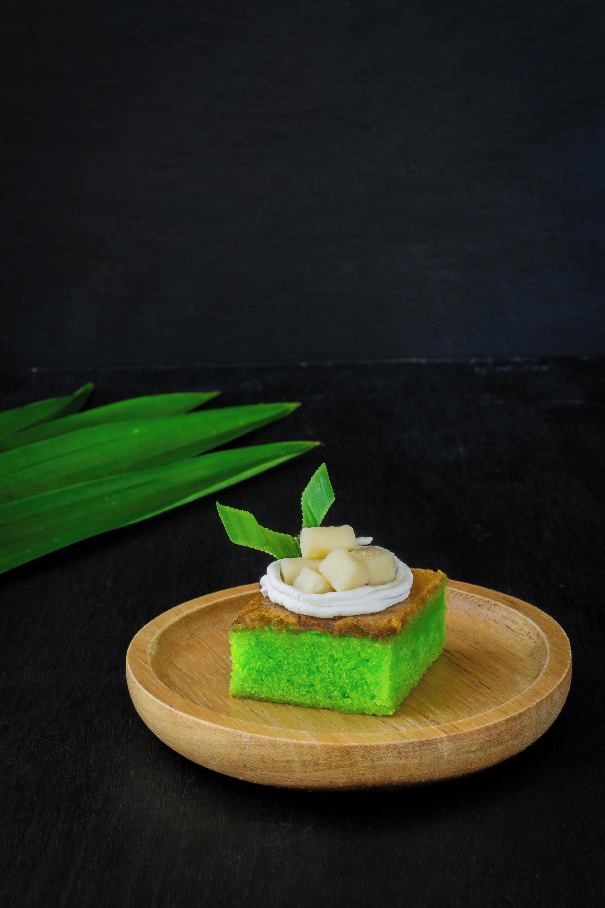 A slice of cake on a wooden plate with a dark background.