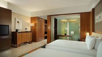 A hotel room with a bed, a TV, a wooden wardrobe, and a bathroom visible through a glass door.
