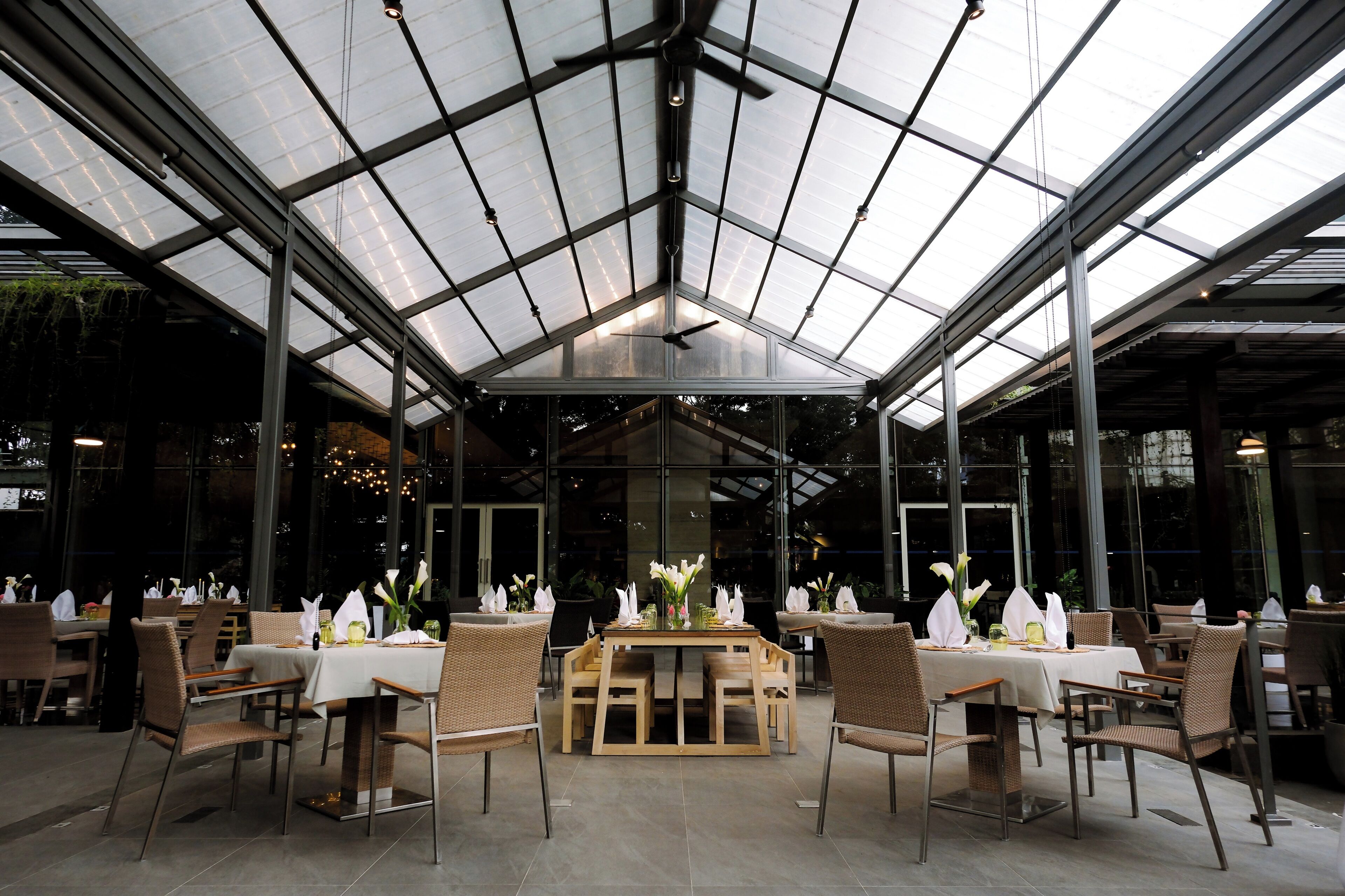 A restaurant with a glass ceiling, tables with white tablecloths, and wicker chairs.