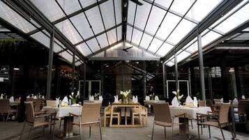 A restaurant with a glass ceiling, tables with white tablecloths, and wicker chairs.